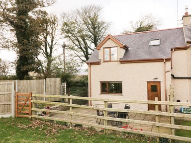 The exterior of a house with a fenced patio area and outdoor furniture surrounded by trees and grass at Bodneithior in Llanerchymedd