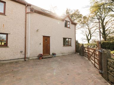 A paved driveway with a wooden gate and a beige house with wooden door and windows at Bodneithior in Llanerchymedd