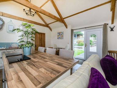A kitchen and dining area with exposed wooden beams a wooden table and a door leading outside at Warbrook in Bradworthy