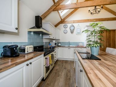 A kitchen with wooden countertops white cabinets a stove a coffee machine a toaster a plant and clocks on the wall at Warbrook in Bradworthy