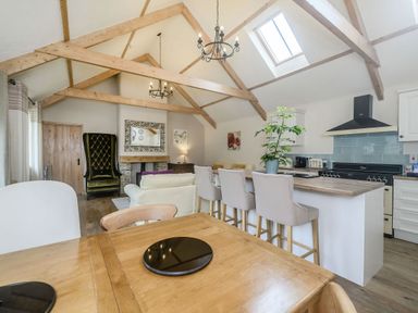A living room with exposed wooden beams a kitchen island with chairs and a dining table at Warbrook in Bradworthy