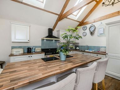 A kitchen with wooden countertops white cabinets clocks on the wall and a plant on the island at Warbrook in Bradworthy