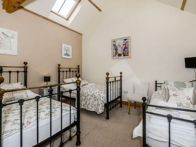 A bedroom with three metal single beds a small white chair and framed pictures on the walls at Warbrook in Bradworthy