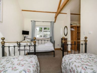 A bedroom with two single beds, a daybed, a small wall-mounted TV, a window with curtains, and an open closet at Warbrook in Bradworthy