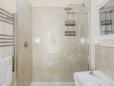 A bathroom with a glass-enclosed shower a metal shower caddy a white sink a mirror and a towel rack with white towels at Warbrook in Bradworthy
