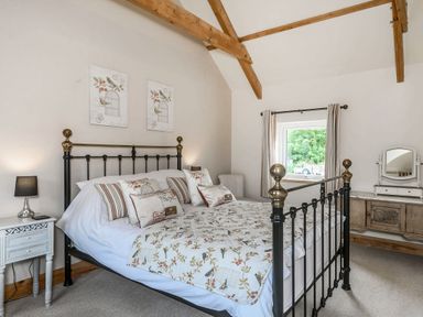A bedroom with a metal bed frame cushions bedside table and a dresser with a mirror at Warbrook in Bradworthy