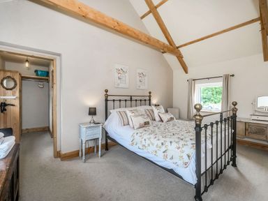 A bedroom with a metal bed frame wooden beams on the ceiling bedside table and a window at Warbrook in Bradworthy