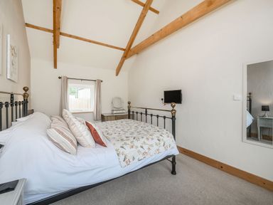 A bedroom with a bed pillows and blanket a wall mounted tv window with curtains a dresser with mirror and wall mirror at Warbrook in Bradworthy