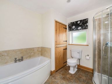 A bathroom with a bathtub toilet shower wooden cabinet and tiled floor at Warbrook in Bradworthy