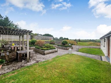 An outdoor garden area with wooden pergola and benches raised flower beds and a grassy lawn at Warbrook in Bradworthy