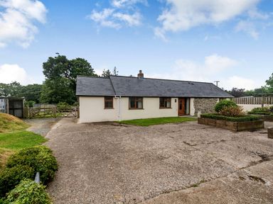 A one-story house with a tiled roof and small garden beds in front at Warbrook in Bradworthy