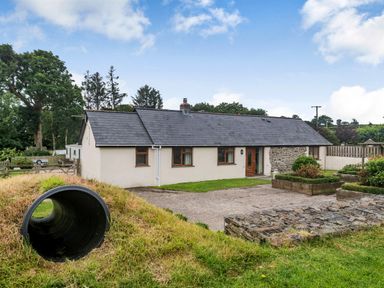 A single story house with a slate roof and a grass lawn with a tunnel at Warbrook in Bradworthy