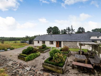 A courtyard with raised garden beds and wooden benches next to a single story house at Warbrook in Bradworthy