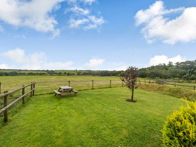 A fenced grassy yard with a picnic table and a small tree overlooking fields at Warbrook in Bradworthy