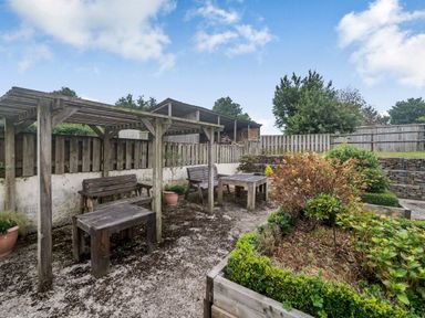 An outdoor garden seating area with wooden benches tables and pergolas near raised plant beds at Warbrook in Bradworthy