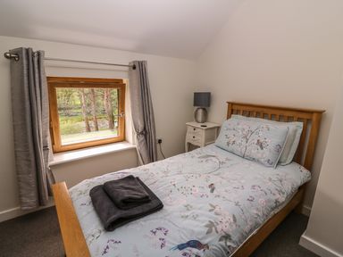 A bedroom with a wooden bed a bedside table with a lamp and a window with curtains at The Farmhouse in Capel Bangor near Aberystwyth