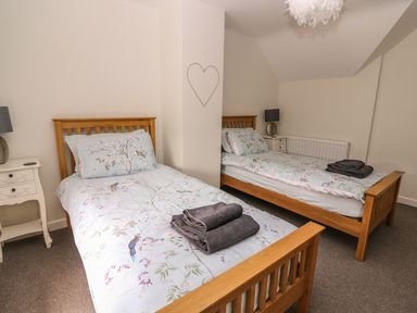 A bedroom with two single wooden beds with floral bedding and folded towels at The Farmhouse in Capel Bangor near Aberystwyth