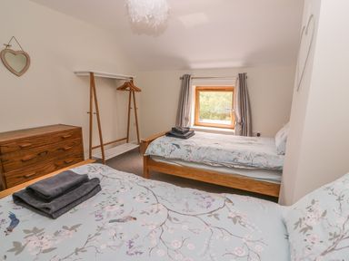 A bedroom with two single beds a wooden dresser a clothes rack and a window at The Farmhouse in Capel Bangor near Aberystwyth