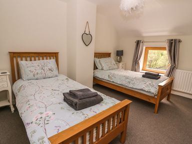 A bedroom with two single wooden beds and a window with curtains at The Farmhouse in Capel Bangor near Aberystwyth