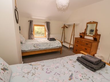 A bedroom with two single beds a wooden dresser a wooden clothes rack and a window with curtains at The Farmhouse in Capel Bangor near Aberystwyth