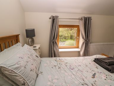A bedroom with a wooden bed a bedside table with a lamp and a window with curtains at The Farmhouse Capel Bangor near Aberystwyth