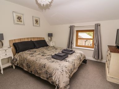 A bedroom with a bed and black and beige bedding two bedside tables with lamps a window with curtains and a chest of drawers with a television at The Farmhouse in Capel Bangor near Aberystwyth