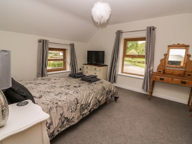A bedroom with a bed a TV on a chest of drawers and a dressing table at The Farmhouse in Capel Bangor near Aberystwyth