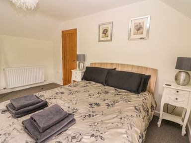 A bedroom with a bed covered with floral patterned bedding two bedside tables with lamps and folded towels on the bed at The Farmhouse in Capel Bangor near Aberystwyth