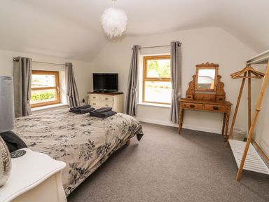 A bedroom with a bed a dresser a wooden vanity and a clothes rack at The Farmhouse in Capel Bangor near Aberystwyth