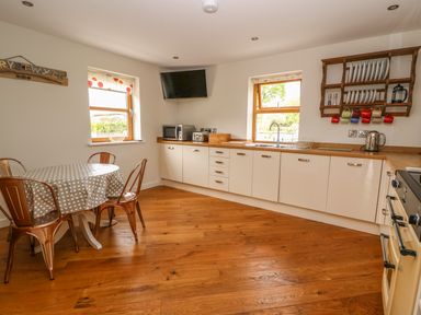 A kitchen with wooden floor a round table with four chairs white cabinets a wall-mounted tv and a dish rack at The Farmhouse in Capel Bangor near Aberystwyth