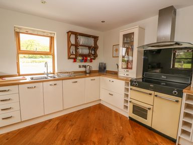 A kitchen with white cabinets wooden countertops a double sink a stove and a wooden plate rack at The Farmhouse in Capel Bangor near Aberystwyth
