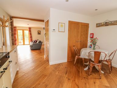 A kitchen area with a round table and four metal chairs with a vase of flowers on the table and a living room with a gray sofa near glass doors at The Farmhouse in Capel Bangor near Aberystwyth