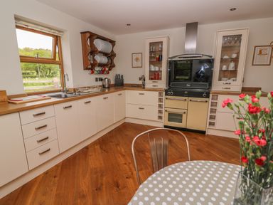A kitchen with white cabinets wooden countertops a window a stove and a table with flowers at The Farmhouse in Capel Bangor near Aberystwyth