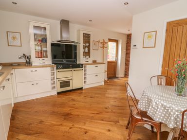 A kitchen with wooden floor cabinets a stove a table with a polka dot tablecloth and chairs at The Farmhouse in Capel Bangor near Aberystwyth
