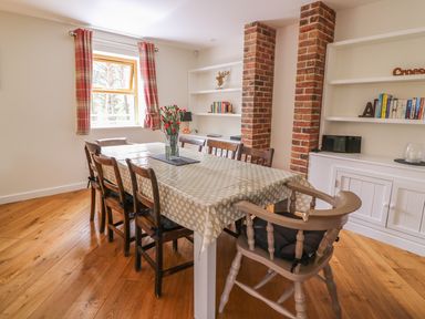 A dining room with a table and chairs near a window with red plaid curtains and brick pillars at The Farmhouse in Capel Bangor near Aberystwyth