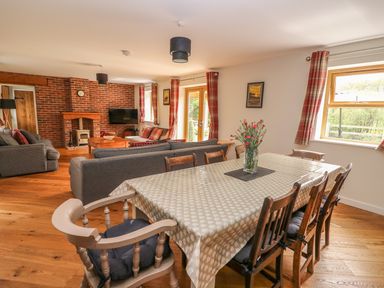 A dining table with chairs and flowers in a living room with sofas and a brick fireplace at The Farmhouse in Capel Bangor near Aberystwyth