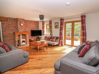 A living room with two gray sofas a wooden coffee table a wood burning stove and glass doors leading outside at The Farmhouse in Capel Bangor near Aberystwyth