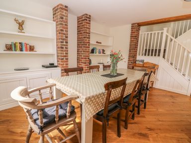 A dining room with a table covered by a tablecloth and chairs around it next to bookshelves and a staircase at The Farmhouse in Capel Bangor near Aberystwyth