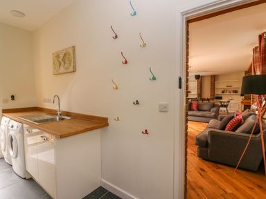 A utility room with a washing machine sink and colorful wall hooks next to a living room with sofas and a floor lamp at The Farmhouse in Capel Bangor near Aberystwyth