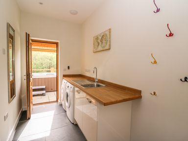 A utility room with a sink washing machine and dryer and colorful hooks on the wall at The Farmhouse in Capel Bangor near Aberystwyth