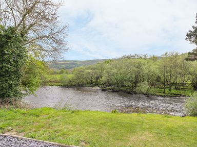 A river bordered by trees and grass with hills in the background at The Farmhouse in Capel Bangor near Aberystwyth