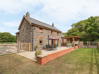 A stone farmhouse with a patio table and chairs under an umbrella and a covered hot tub in a garden at The Farmhouse in Capel Bangor near Aberystwyth