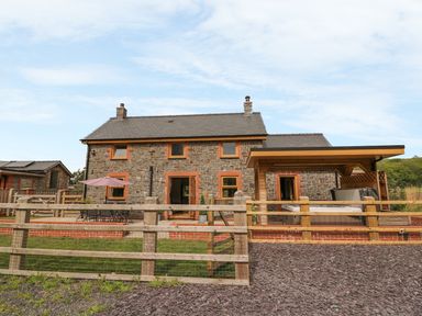Exterior view of a stone house with a patio table umbrella wooden fence and covered hot tub at The Farmhouse in Capel Bangor near Aberystwyth