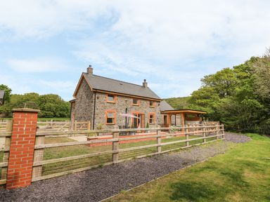 A stone house with a fenced yard and patio furniture surrounded by trees at The Farmhouse in Capel Bangor near Aberystwyth