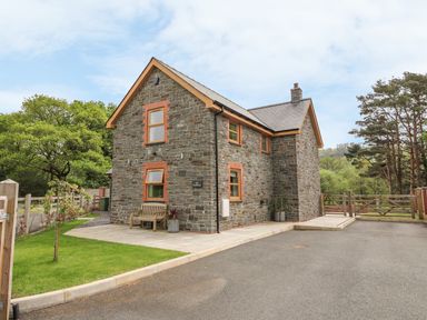 A stone house with a bench and potted plants outside near trees and a gate at The Farmhouse in Capel Bangor near Aberystwyth