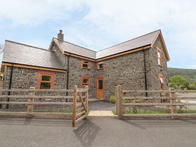A stone house with wooden framed windows and a wooden gate in front at The Farmhouse in Capel Bangor near Aberystwyth