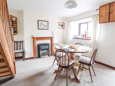 A dining area with a round wooden table and four chairs near a window and a fireplace at Haulfryn in Bethesda