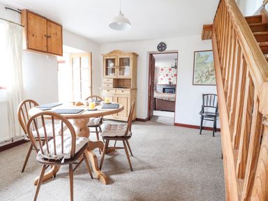 A dining room with a wooden table and four chairs next to a wooden cabinet and wooden staircase at Haulfryn in Bethesda