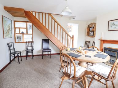 A dining room with a round wooden table and chairs near a staircase and fireplace at Haulfryn Bethesda