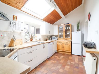 A kitchen with white cabinets wooden countertops a wooden cupboard a white fridge and a skylight at Haulfryn Bethesda